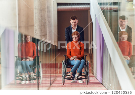 A company director assists his business colleague in a wheelchair, helping her navigate to their startup office, where they work alongside their diverse team of colleagues, emphasizing inclusivity and 120450586