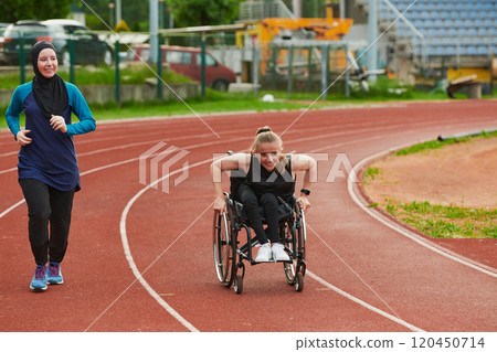 A Muslim woman in a burqa running together with a woman in a wheelchair on the marathon course, preparing for future competitions. 120450714