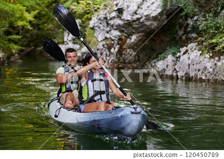 A young couple enjoying an idyllic kayak ride in the middle of a beautiful river surrounded by forest greenery 120450789