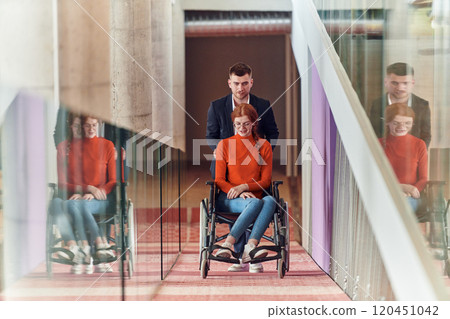 A company director assists his business colleague in a wheelchair, helping her navigate to their startup office, where they work alongside their diverse team of colleagues, emphasizing inclusivity and A company director assists his business colleague in a wheelchair, helping her navigate to their startup office, where they work alongside their diverse team of colleagues, emphasizing inclusivity and 120451042