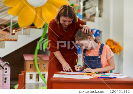 Creative kids during an art class in a daycare center or elementary school classroom drawing with female teacher. 120451112