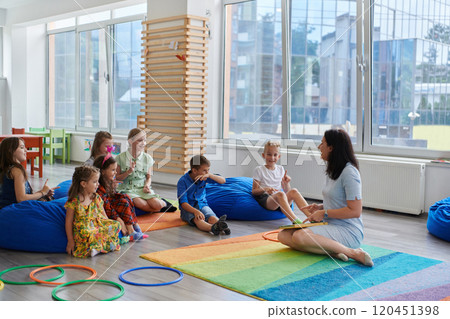 Reading time in an elementary school or kindergarten, a teacher reads a book to children in an elementary school or kindergarten. The concept of pre-school education. Selective focus 120451398