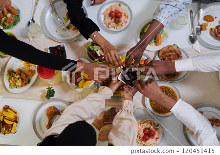 Top view of diverse hands of a Muslim family delicately grasp fresh dates, symbolizing the breaking of the fast during the holy month of Ramadan, capturing a moment of cultural unity, shared tradition 120451415