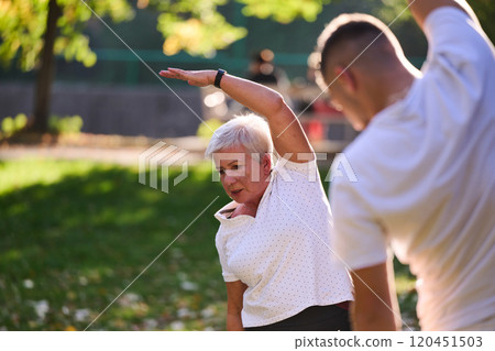 A group of seniors follows a trainer, engaging in outdoor exercises in the park, as they collectively strive to maintain vitality and well-being, embracing an active and health-conscious lifestyle in 120451503