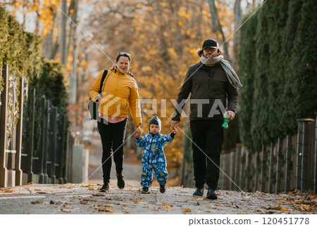 A loving couple strolls through a sunlit park with their young son, surrounded by the vibrant colors of autumn, enjoying a joyful and peaceful family moment together. A loving couple strolls through a sunlit park with their young son, surrounded by the vibrant colors of autumn, enjoying a joyful and peaceful family moment together. 120451778