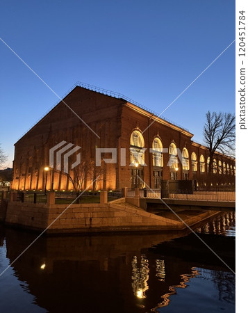 Illuminated Brick Building by the River at Dusk with Reflections Illuminated Brick Building by the River at Dusk with Reflections 120451784