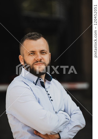 A successful young businessman in a shirt, with crossed arms, poses outdoors, confident expression on his face. A successful young businessman in a shirt, with crossed arms, poses outdoors, confident expression on his face. 120452051