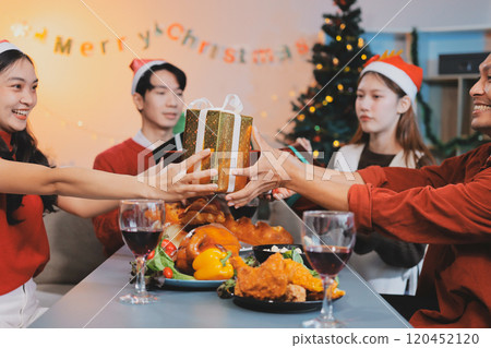 Group of young Asian man and women as friends having fun at a New Year's celebration, holding gift boxes standing by Christmas tree decoration, midnight countdown Party at home with holiday season. Group of young Asian man and women as friends having fun at a New Year's celebration, holding gift boxes standing by Christmas tree decoration, midnight countdown Party at home with holiday season. 120452120