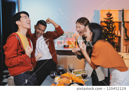 Group of young Asian man and women as friends having fun at a New Year's celebration, holding gift boxes standing by Christmas tree decoration, midnight countdown Party at home with holiday season. 120452129
