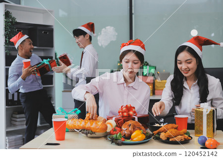 full length view of a group of business team wearing red Santa hat and exchange gift box together in the office for Christmas. 120452142