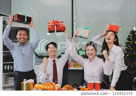 full length view of a group of business team wearing red Santa hat and exchange gift box together in the office for Christmas. 120452155