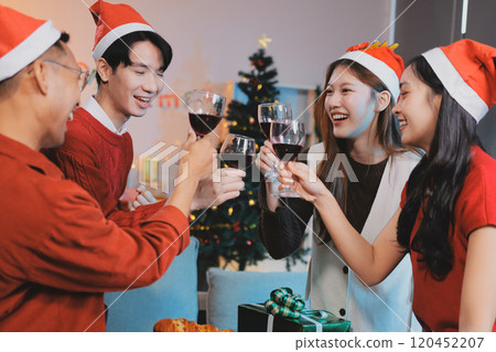 Group of young Asian man and women as friends having fun at a New Year's celebration, holding gift boxes standing by Christmas tree decoration, midnight countdown Party at home with holiday season. 120452207