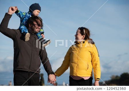 A happy family strolls along a chilly autumn beach, with their young son joyfully running ahead, creating lasting memories as the crisp wind and soothing waves embrace them in a moment of pure 120452360