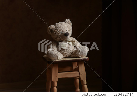 Lonely teddy bear sitting on a chair. A lone Teddy bear sitting in the dark, side view, forgotten toy 120452714