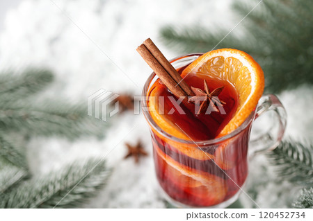 Mulled wine in glass glasses decorated with cinnamon sticks on snow wooden table, nearby are green spruce branches. Christmas drink, New Year's punch. Mulled wine in glass glasses decorated with cinnamon sticks on snow wooden table, nearby are green spruce branches. Christmas drink, New Year's punch. 120452734
