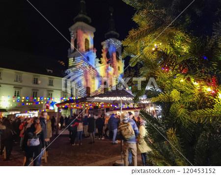 People at a Christmas market with beautiful lights decorations and Mariahilfer church , at night, in the city center of Graz, Styria region, Austria 120453152