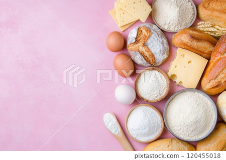 Various baking ingredients including flour, eggs, cheese, and bread on a pink surface 120455018
