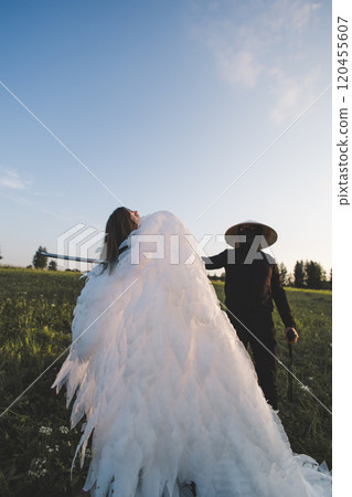 A samurai kills an angel with a katana in a vast grassy field under a clear blue sky, creating a dramatic contrast between light and dark. A samurai warrior with a katana stabs a snow-white angel. 120455607