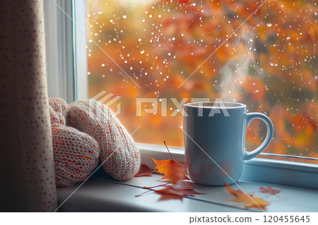 A cozy autumn scene with an open window, showcasing colorful leaves and falling raindrops outside, while inside there's steam rising from the coffee mug on the windowsill. A cozy autumn scene with an open window, showcasing colorful leaves and falling raindrops outside, while inside there's steam rising from the coffee mug on the windowsill. 120455645