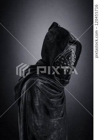 Scary figure in hooded cloak with spike studs mask at night over dark misty background 120455716