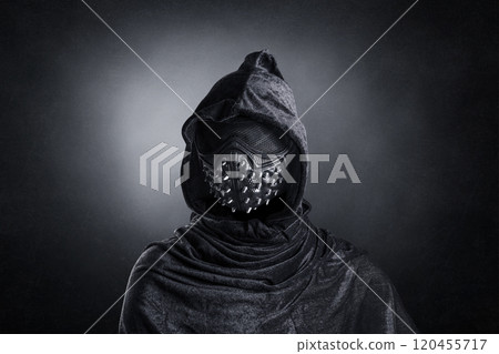 Scary figure in hooded cloak with spike studs mask at night over dark misty background 120455717
