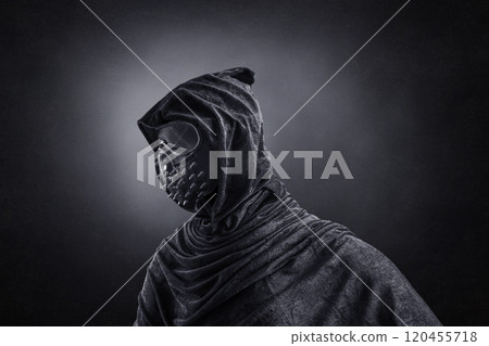 Scary figure in hooded cloak with spike studs mask at night over dark misty background Scary figure in hooded cloak with spike studs mask at night over dark misty background 120455718