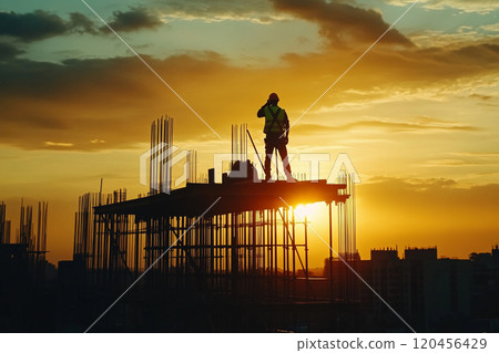 Silhouette of a construction worker working on top of a building at sunset. 120456429