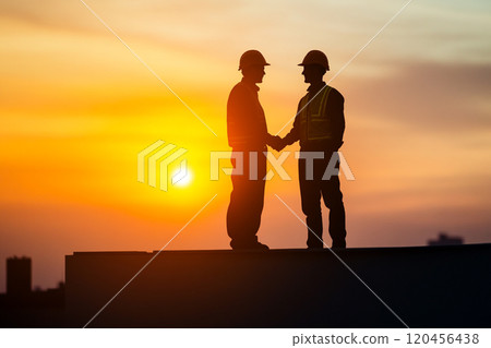 Silhouette of a construction worker working on top of a building at sunset. 120456438