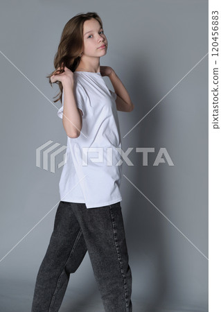 A young girl in a white t-shirt and jeans poses with a subtle yet confident stance, emphasizing self-expression and strength. The image highlights casual style and a determined outlook. 120456883