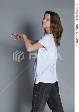 A girl strikes a confident pose, with her hand gripping her shirt, looking directly into the camera. The minimalist setting enhances the focus on her self-assured presence and casual fashion. A girl strikes a confident pose, with her hand gripping her shirt, looking directly into the camera. The minimalist setting enhances the focus on her self-assured presence and casual fashion. 120456884