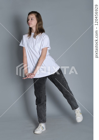 A girl poses in a relaxed stance, leaning slightly while dressed in a white t-shirt and jeans. The simplicity of her outfit and posture reflects the laid-back nature of youth today. 120456929