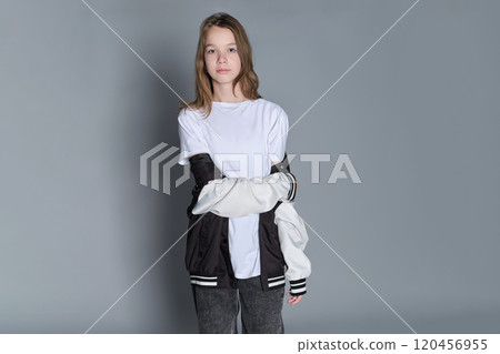 A teenage girl in a relaxed, modern outfit holds her jacket, conveying a sense of style and freedom. This image reflects the trend of embracing casual fashion as a form of personal expression. A teenage girl in a relaxed, modern outfit holds her jacket, conveying a sense of style and freedom. This image reflects the trend of embracing casual fashion as a form of personal expression. 120456955