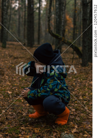 A child lost in the forest wipes his face from tears with his hand. A lost child cries and squats in the forest wearing orange boots feeling scared and alone in this wilderness. 120457612