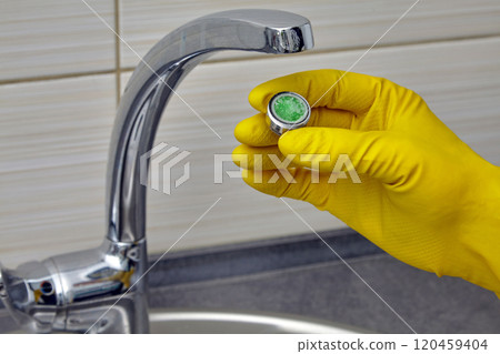 person in yellow rubber gloves changing clogged faucet aerator 120459404