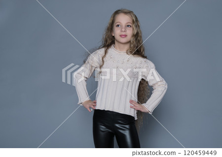 A girl strikes a confident pose in her sweater and dark leggings, exuding natural charm. This portrait highlights the blend of casual style and quiet confidence found in young individuals. 120459449