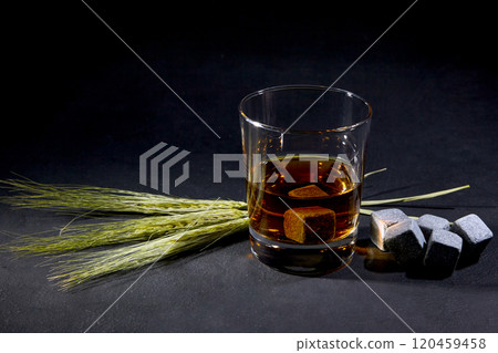 glass of whiskey with stone cubes and rye ears on black concrete table glass of whiskey with stone cubes and rye ears on black concrete table 120459458
