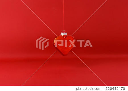 Red heart-shaped ornament hanging on string, solid red background, festive holiday decoration, visually striking, perfect for Valentine's Day or Christmas, love-themed decor, elegant and simple 120459470