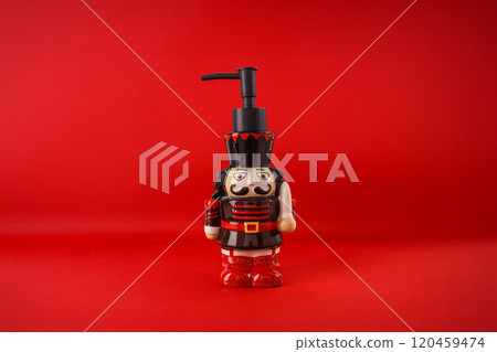 a soap dispenser designed to look like a toy soldier or nutcracker. a black pump on top, The background is a solid red color, a festive and decorative design, for use during the holiday season 120459474