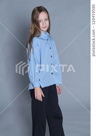 A young girl in a light blue shirt and black pants stands confidently with a gentle smile, her head slightly tilted. The photo emphasizes her youthful charm and relaxed confidence. 120459580