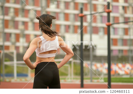 A confident woman in sports attire smiles over her shoulder, her hair flowing, showcasing her fitness journey. This photo connects physical health with emotional well-being. 120460311