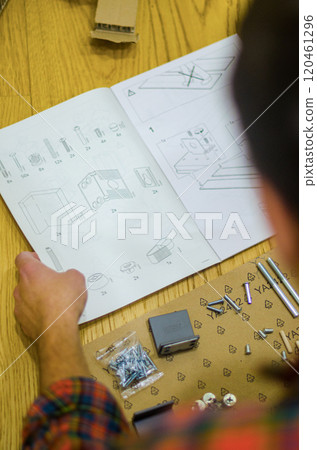 Furniture assembly man holding bolts, furniture assembling instructions and tool. High quality photo Furniture assembly man holding bolts, furniture assembling instructions and tool. High quality photo 120461296