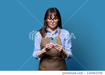 Business woman owner worker in apron using smartphone, on blue background 120462548