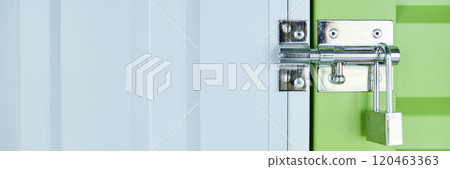 Website header shot of metal latch with lock on green door leading to self storage unit at warehouse, copy space 120463363