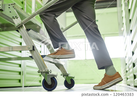 Cropped shot of mans feet stepping on rolling ladder to reach self storage unit with personal belongings at warehouse, copy space 120463383
