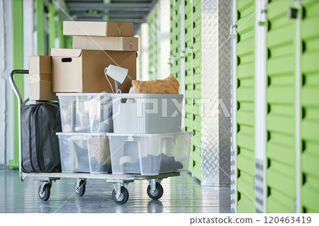 Background shot of cardboard and plastic boxes storing personal belongings loaded on dolly cart next to self storage unit in warehouse during moving out or apartment decluttering, copy space Background shot of cardboard and plastic boxes storing personal belongings loaded on dolly cart next to self storage unit in warehouse during moving out or apartment decluttering, copy space 120463419