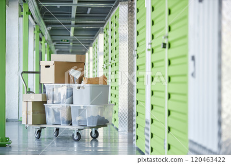Background shot of dolly cart loaded with cardboard boxes storing personal belongings in hallway of self storage warehouse during moving out or apartment decluttering, copy space 120463422