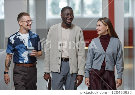 Medium shot of positive African American male boss dressed in smart casual clothes engaged in conversation with employees while walking along business center hallway 120463923