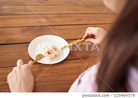 Woman eating dessert with fork and knife on wooden table - close-up dining scene 120464379