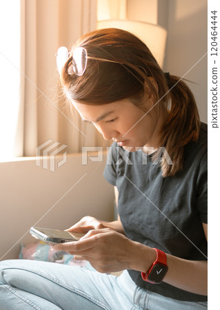 Woman using mobile phone sitting near to the windows with warm sunlight. 120464444