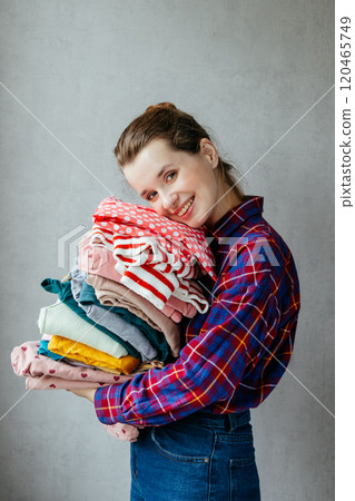 Housewife girl holds stack of clean clothes in hands after washing, drying. Housewife girl holds stack of clean clothes in hands after washing, drying. 120465749